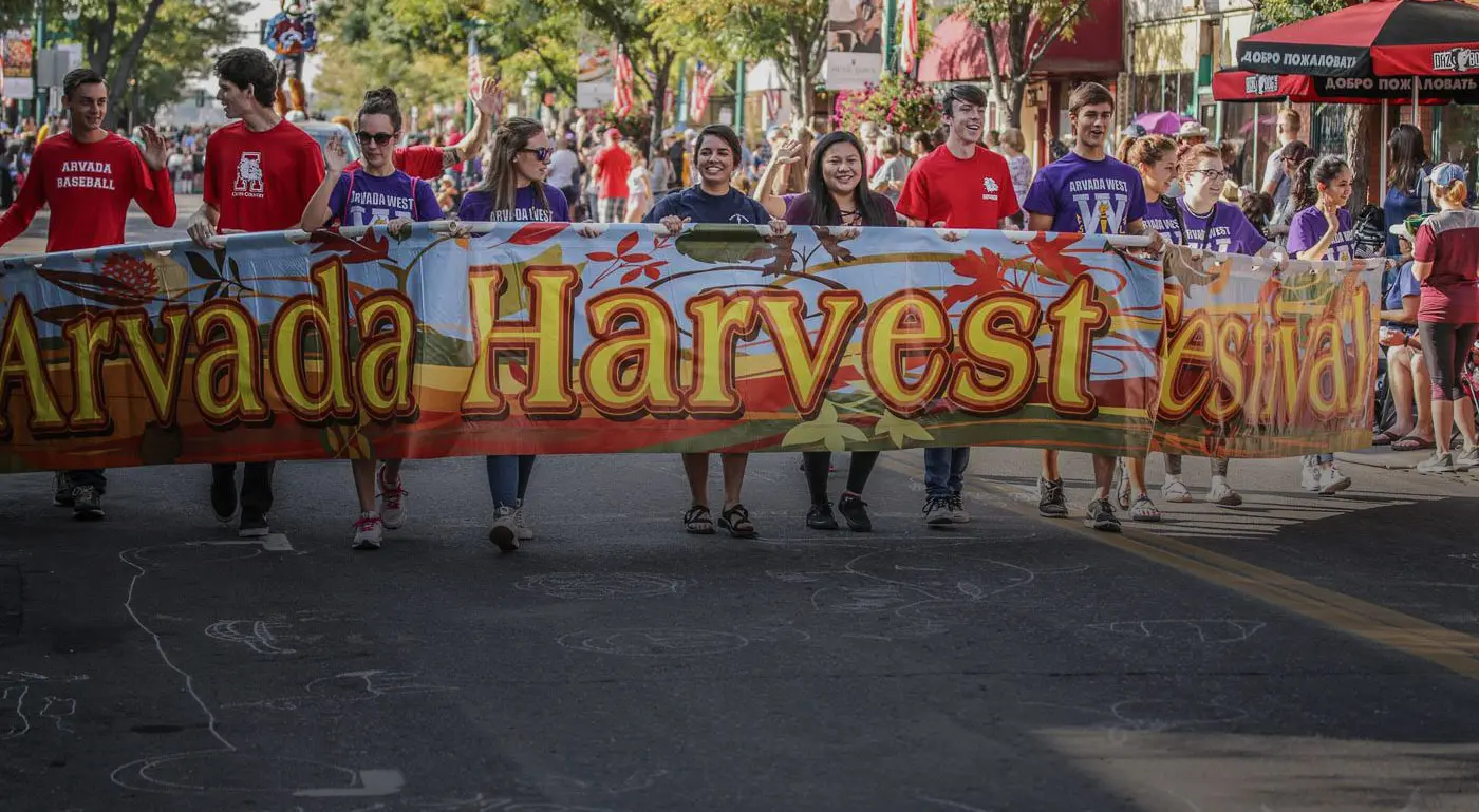 People Holding Arvada Harvest Festival Banner in Hands